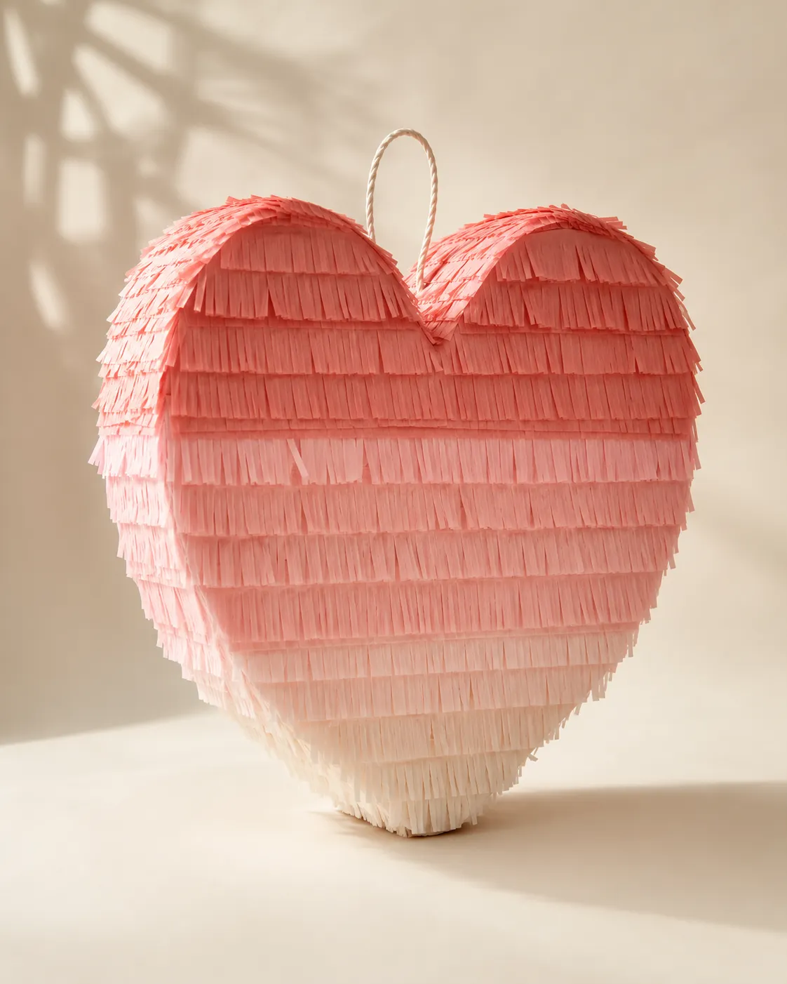 Handcrafted star-shaped piñata with paper fringes in coral and cream tones, against an ivory background